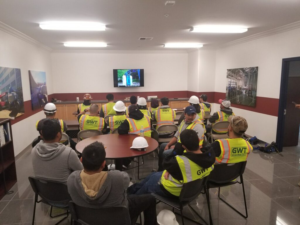 Workers in high-visibility vests watching an aerial lift safety training video in a classroom