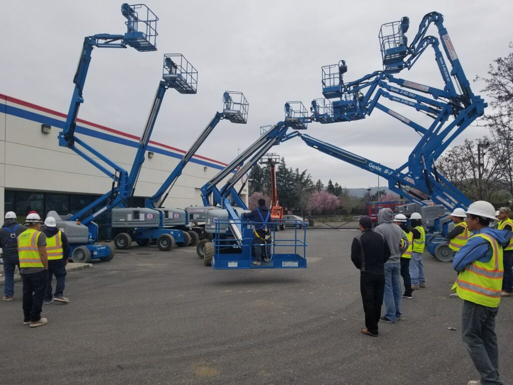 Group watching a demonstration of several raised Genie boom lifts during operator training