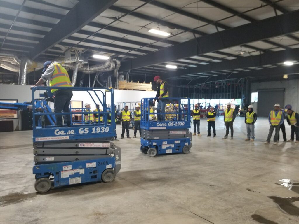 Trainees operating two Genie GS-1930 scissor lifts during hands-on training in a warehouse