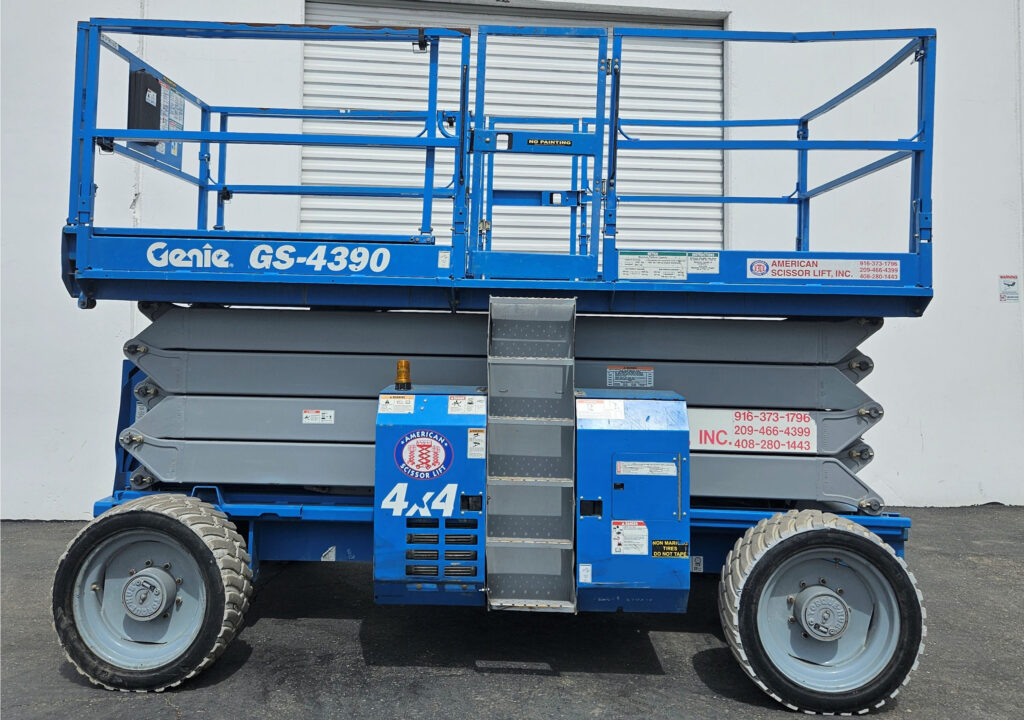 Used 2014 blue Genie GS-4390 4x4 rough terrain scissor lift with its platform lowered in front of an American Scissor Lift building