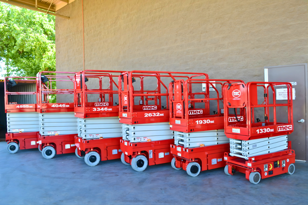 Row of new red MEC electric slab scissor lifts in several sizes parked side by side outside a building