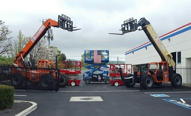 Two JLG telehandlers raised beside a scissor lift displaying an American flag at a branch