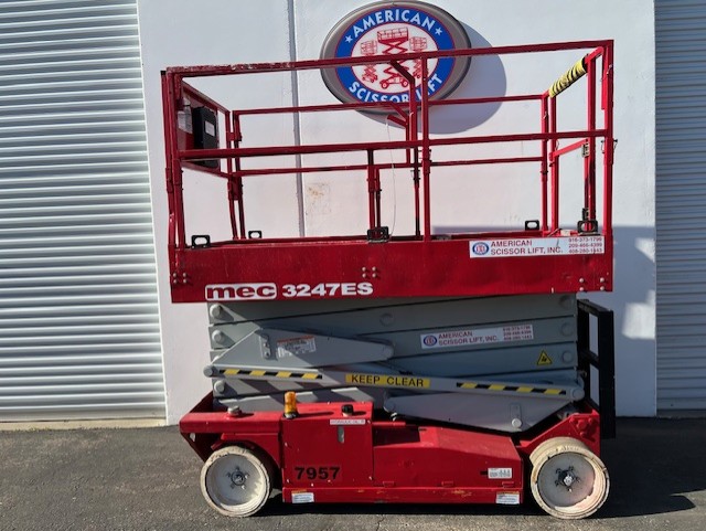 Used 2012 red MEC 3247ES electric scissor lift with its platform lowered in front of an American Scissor Lift building