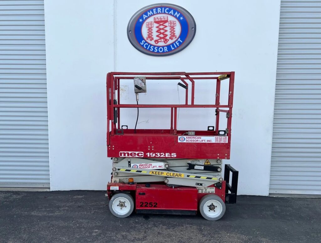 Used 2013 red MEC 1932ES electric scissor lift with its platform lowered in front of an American Scissor Lift building