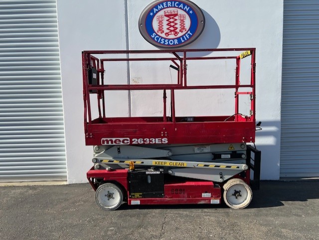 Used 2013 red MEC 2633ES electric scissor lift with its platform lowered in front of an American Scissor Lift building