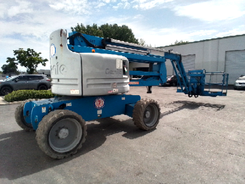 Used 2014 Genie Z-60/34 articulating boom lift with its boom and jib folded, parked in an equipment yard, from the American Scissor Lift rental fleet